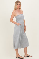 woman wearing a gray strapless jumpsuit with a ruched bodice and pockets, standing sideways