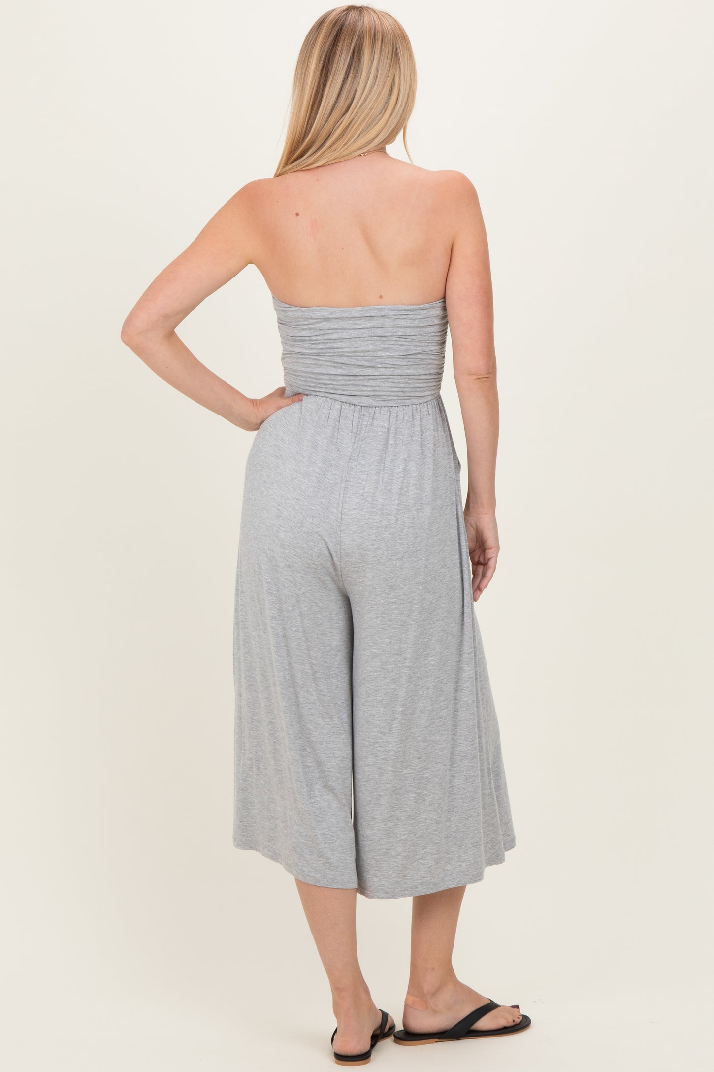 woman wearing a grey strapless jumpsuit with a wide leg and gathered bodice, viewed from the back
