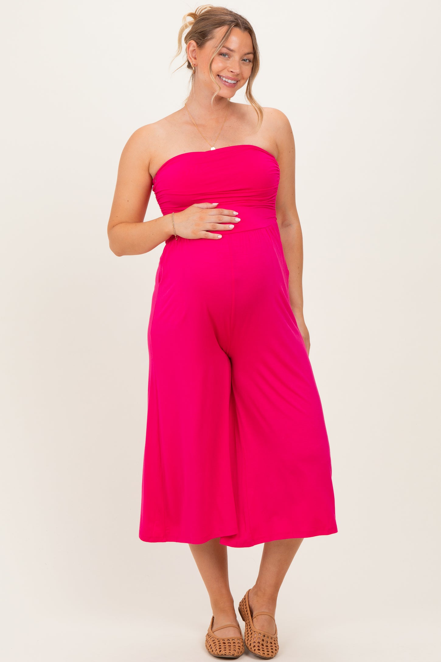 woman wearing a bright pink strapless maternity jumpsuit and holding her baby bump