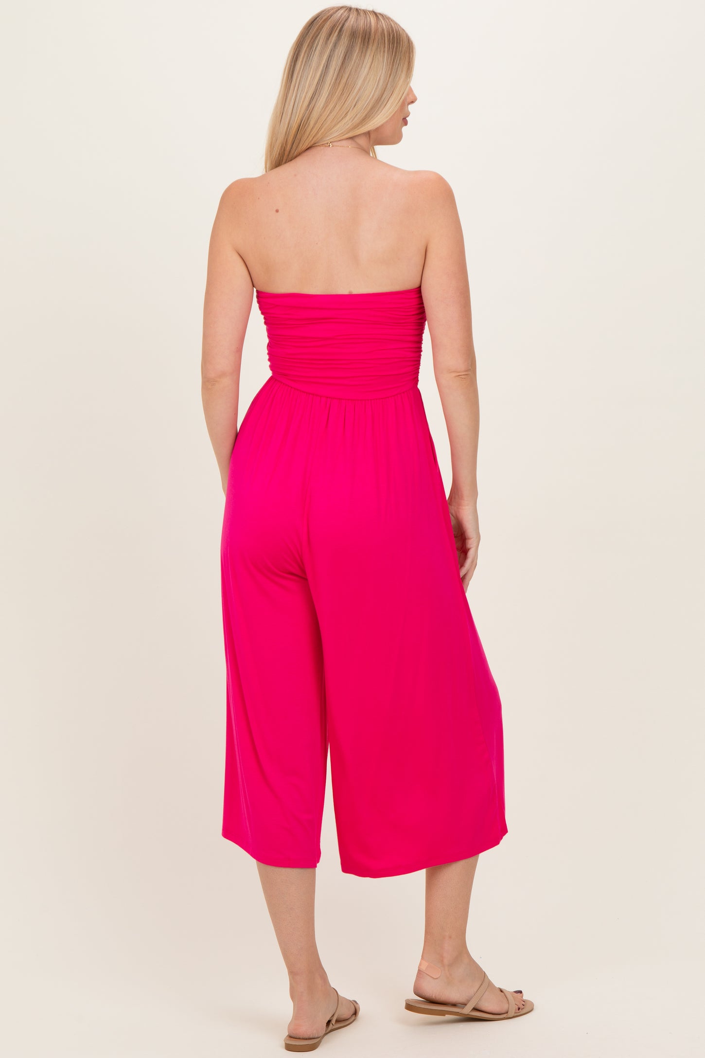 woman wearing a bright pink strapless jumpsuit with a relaxed fit and cropped legs viewed from the back