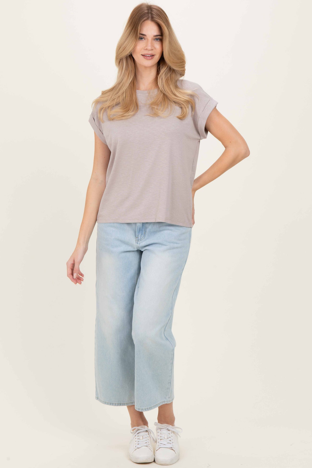 woman wearing a light gray short sleeve top and wide-leg light blue jeans, standing with one hand on her hip