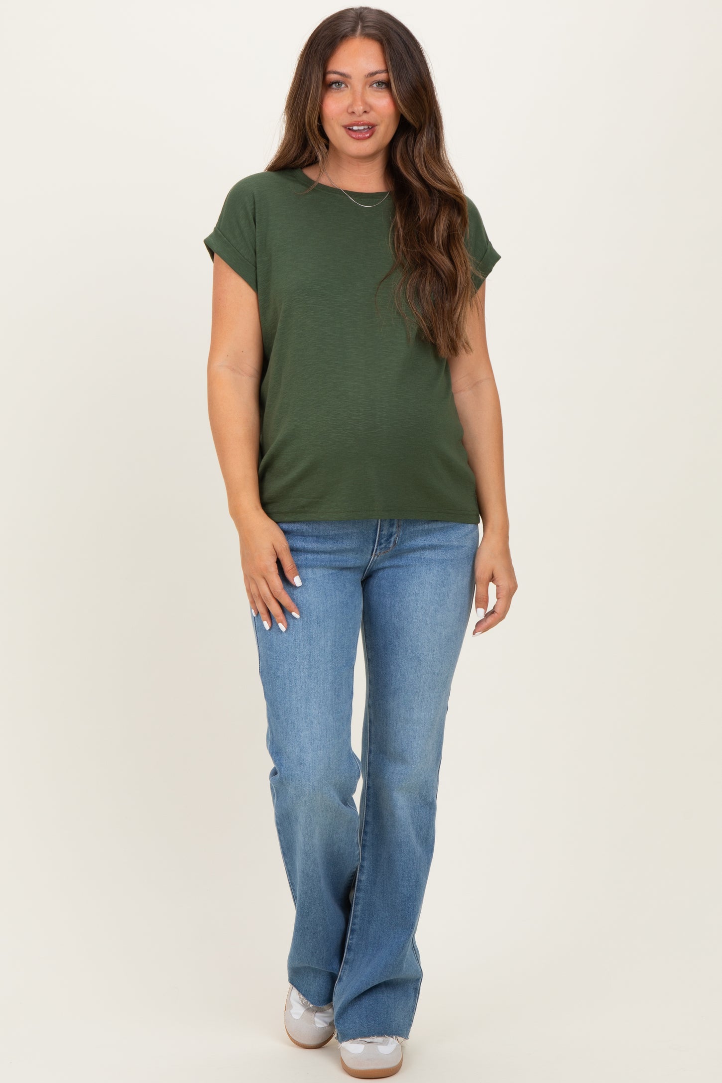 woman wearing a dark green short sleeve maternity top and light blue flared jeans, with no visible baby bump