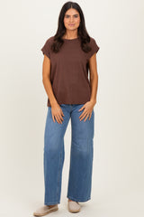 woman wearing a brown short sleeve top and blue wide leg jeans standing against a plain background