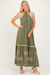 woman wearing an olive green maxi dress with halter neck and floral embroidery at the hem