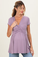 woman wearing a lavender maternity top with a deep v-neck and a gathered bodice, holding her baby bump