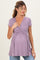 woman wearing a lavender maternity top with a deep v-neck and a gathered bodice, holding her baby bump