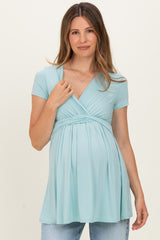 woman wearing a light blue short sleeve maternity top with a gathered waist and a visible baby bump