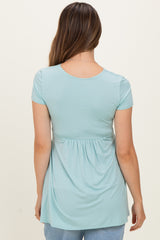 woman wearing a light blue short sleeve maternity top with a gathered waist, showing a relaxed fit from the back