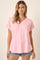 woman wearing a pink v-neck t-shirt with rolled sleeves and a pocket, styled with denim shorts