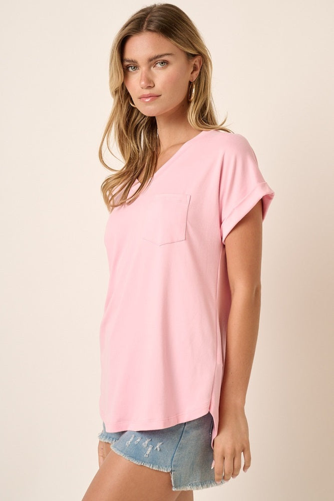 woman wearing a light pink short sleeve top with a pocket and a relaxed fit, paired with denim shorts