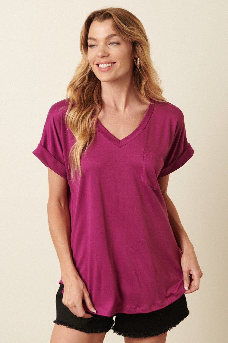 woman wearing a magenta short sleeve v-neck top with a chest pocket and black denim shorts