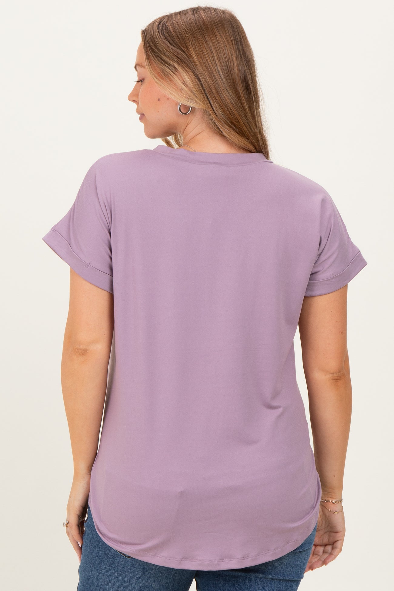 woman wearing a lilac maternity top with short rolled sleeves, showing a relaxed fit and longer back hem