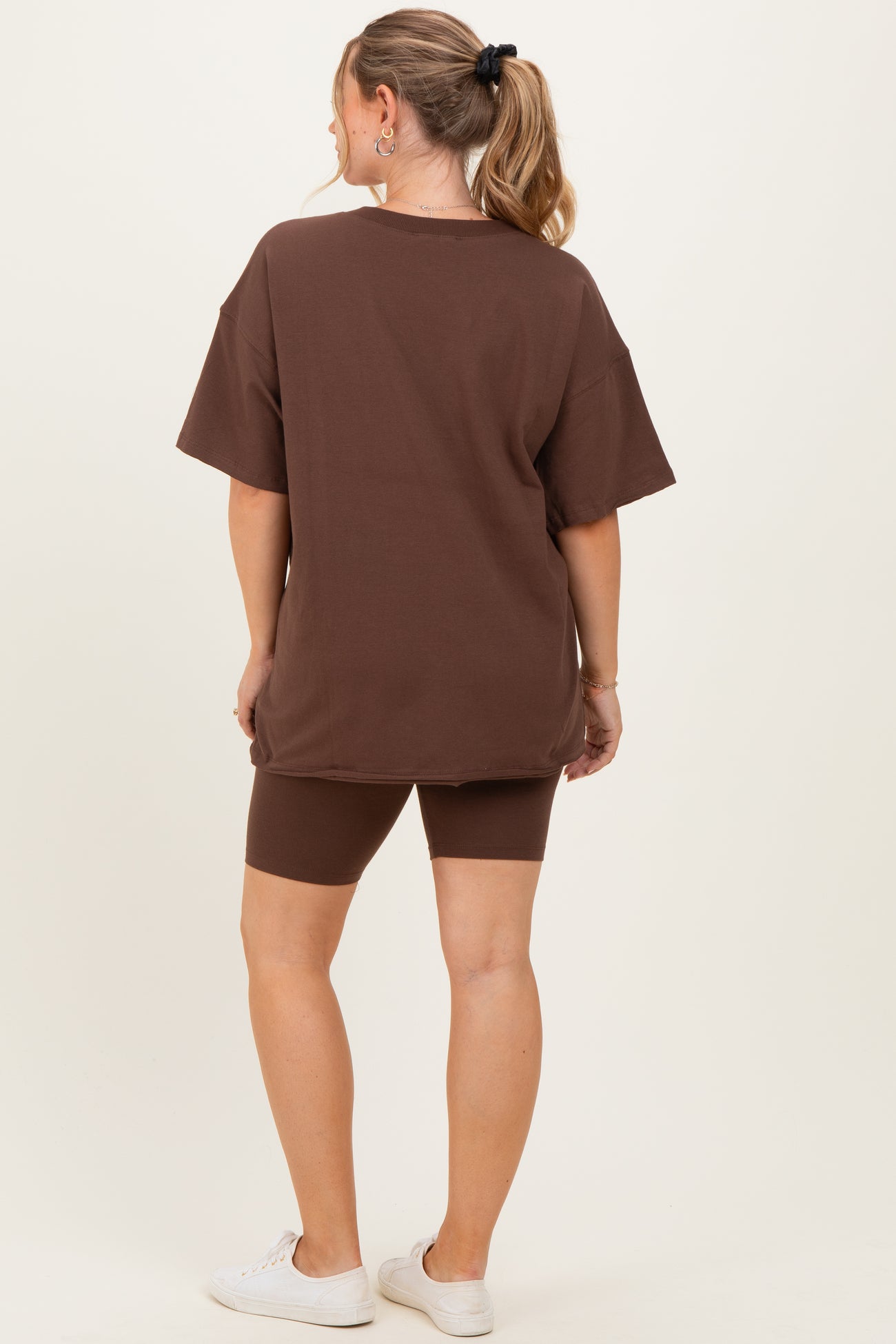 woman wearing a brown oversized t-shirt and matching biker shorts, showing a comfortable maternity outfit from behind