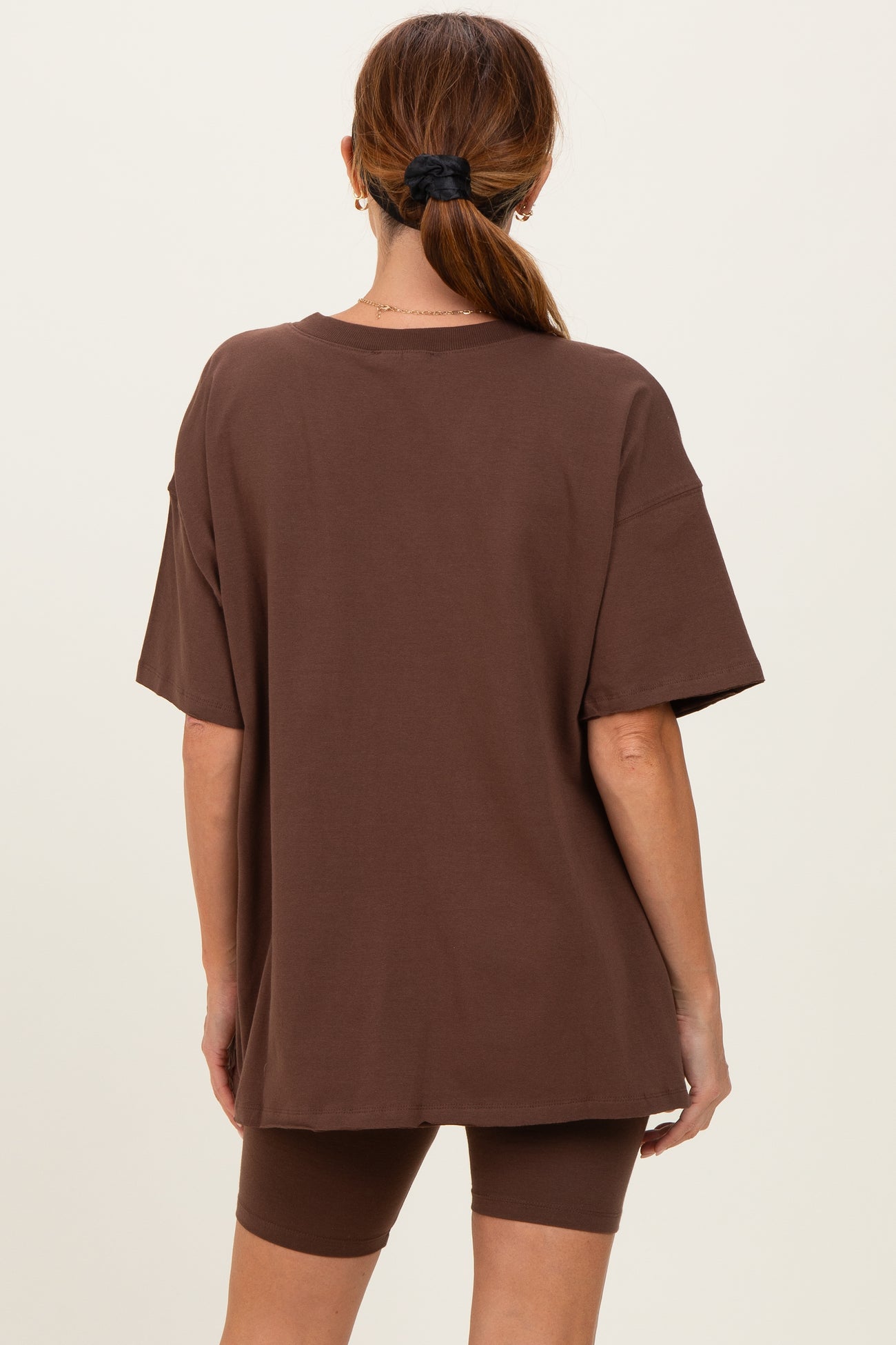 woman wearing a loose fitting brown oversized t-shirt and matching brown bike shorts, seen from the back