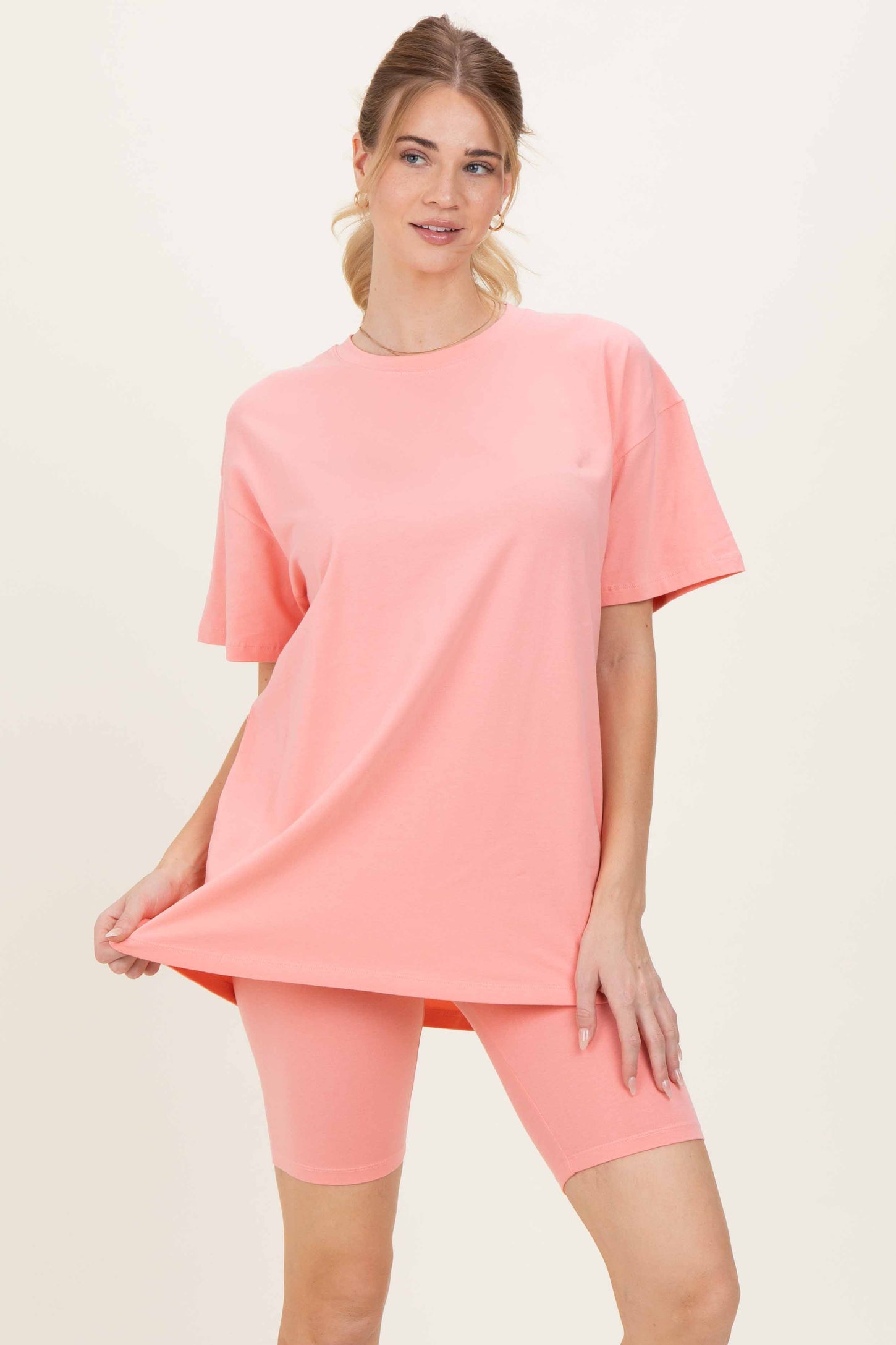 woman wearing a coral oversized t-shirt and matching bike shorts, posing with one hand on the shirt