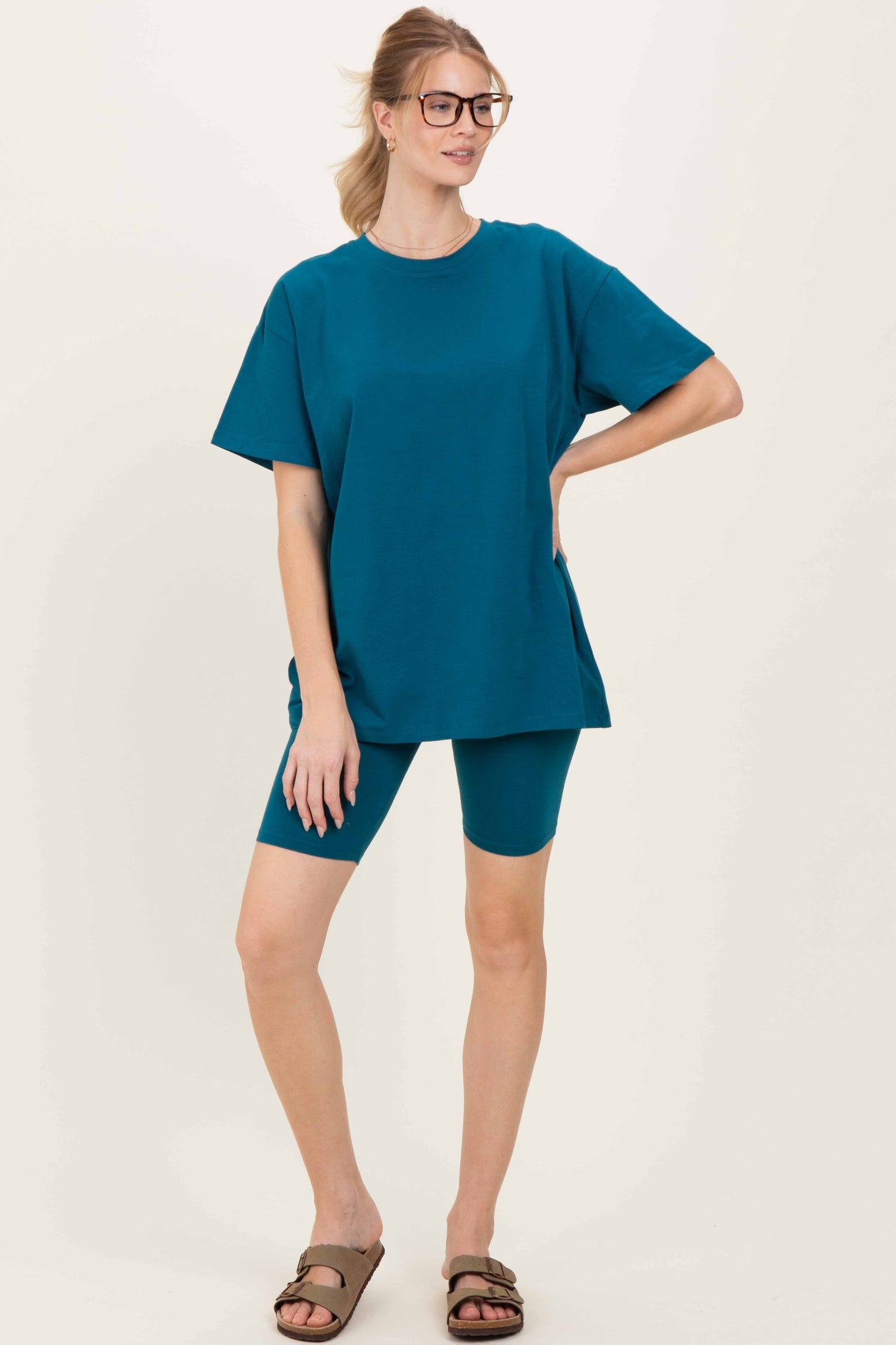 woman wearing a teal oversized t-shirt and matching biker shorts, styled with glasses and sandals