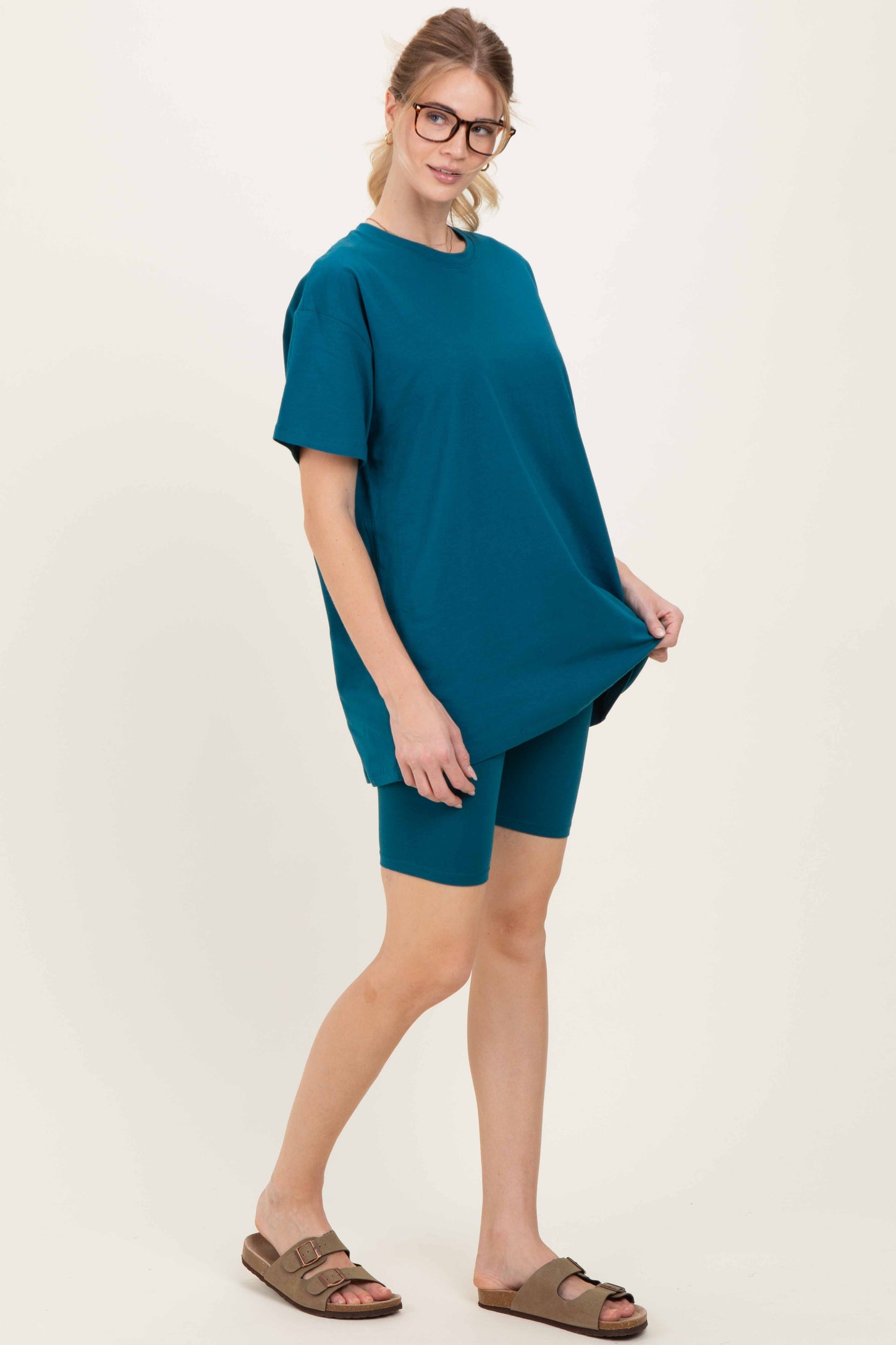 woman wearing a teal oversized t-shirt and matching biker shorts, styled with glasses and sandals