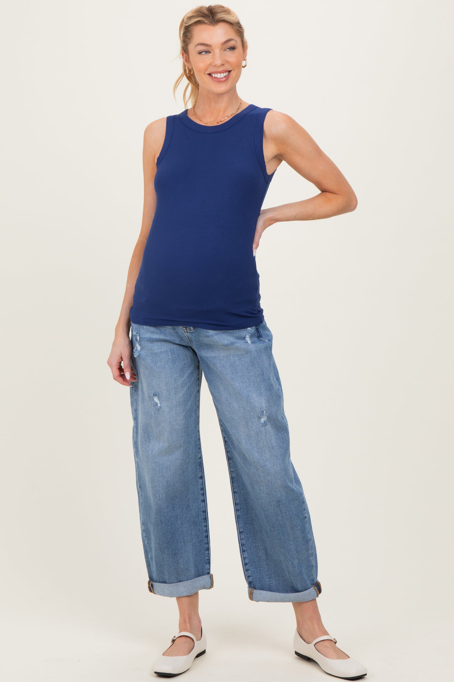 woman wearing a dark blue maternity tank top and distressed light wash jeans, showing her baby bump