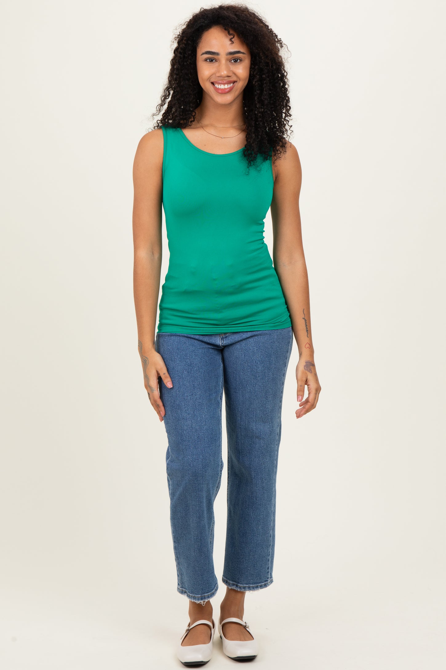 woman wearing a green sleeveless top paired with light blue straight-leg jeans and black slip-on shoes