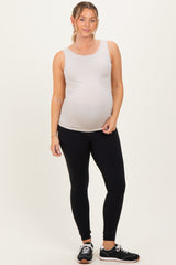 woman wearing a light gray maternity tank top and black maternity leggings, showing her baby bump