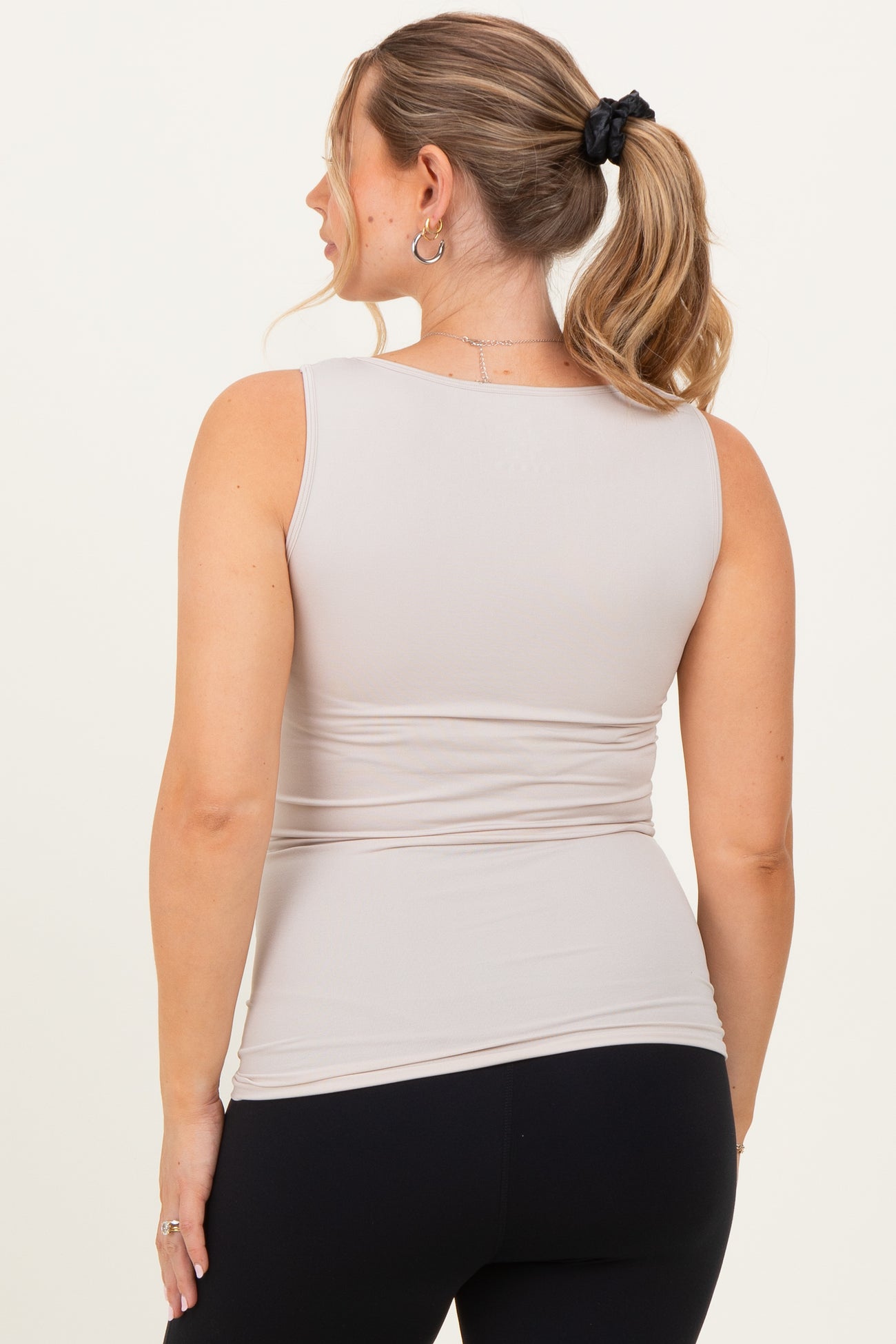 woman wearing a beige maternity tank top with ruched detailing, showing her baby bump from the side