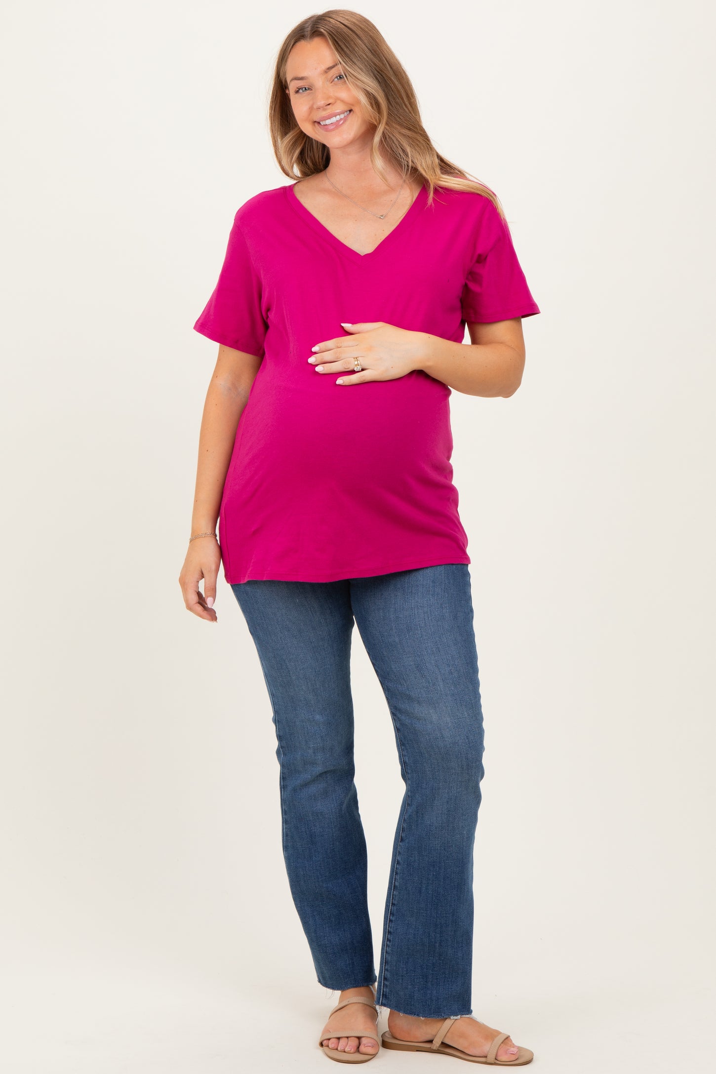 woman wearing a hot pink v-neck maternity top and blue flared jeans, gently holding her baby bump