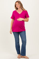 woman wearing a hot pink v-neck maternity top and blue flared jeans, gently holding her baby bump