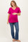 woman wearing a hot pink v-neck maternity top and blue flared jeans, gently holding her baby bump