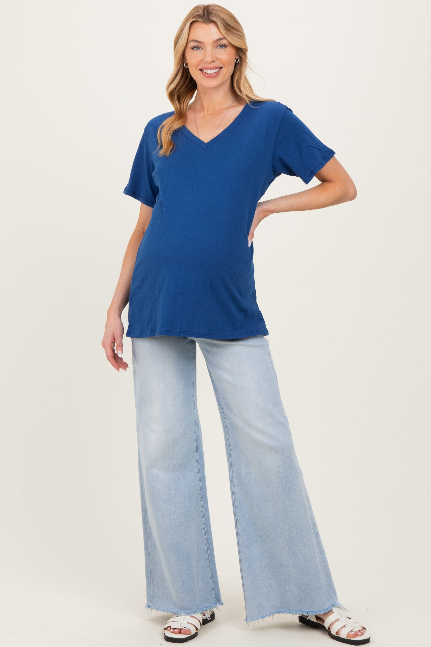 woman wearing a bright blue v-neck maternity top and light wash flared jeans, with a visible baby bump