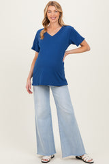 woman wearing a bright blue v-neck maternity top and light wash flared jeans, with a visible baby bump