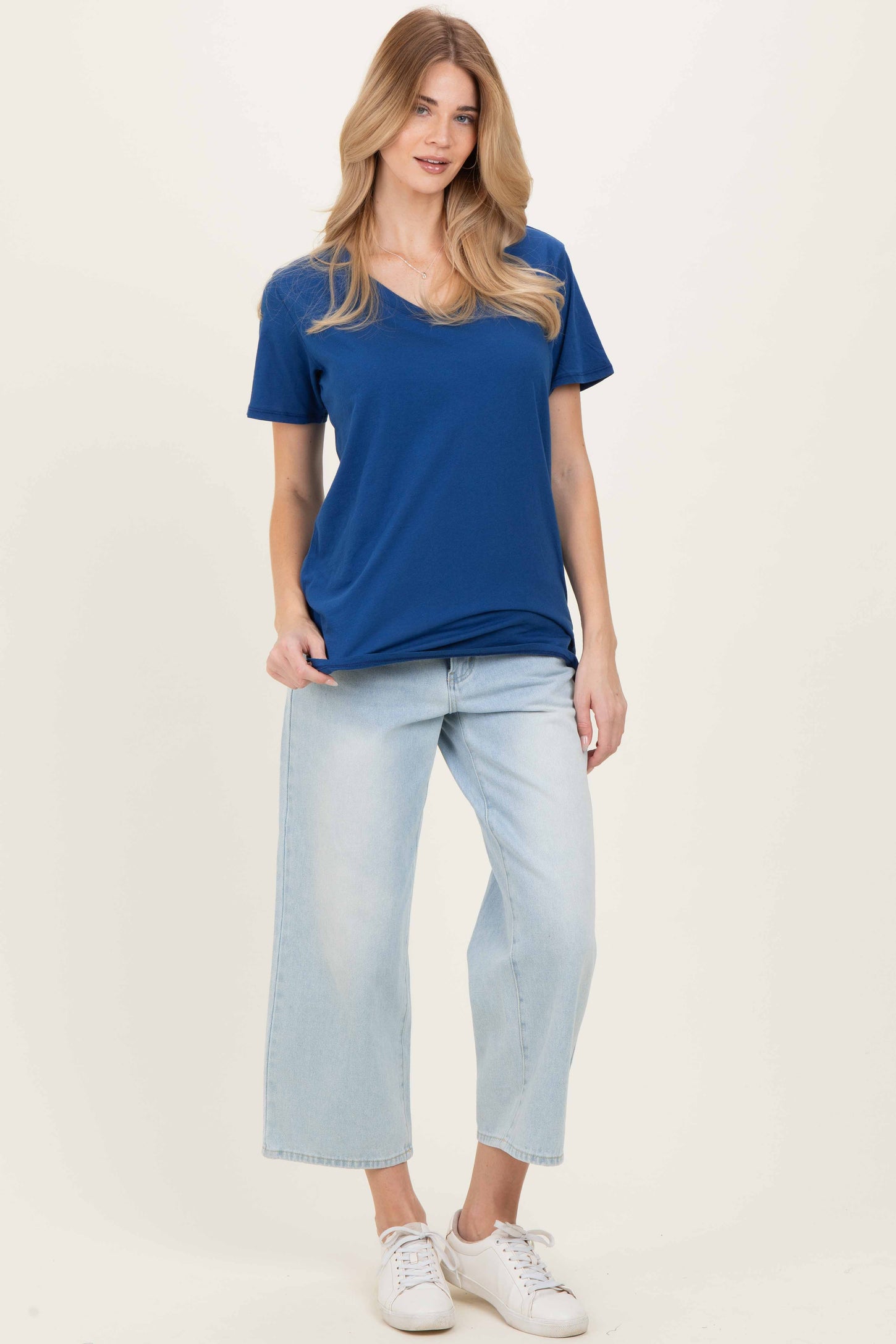 woman wearing a blue v-neck t-shirt and light wash cropped jeans with white sneakers