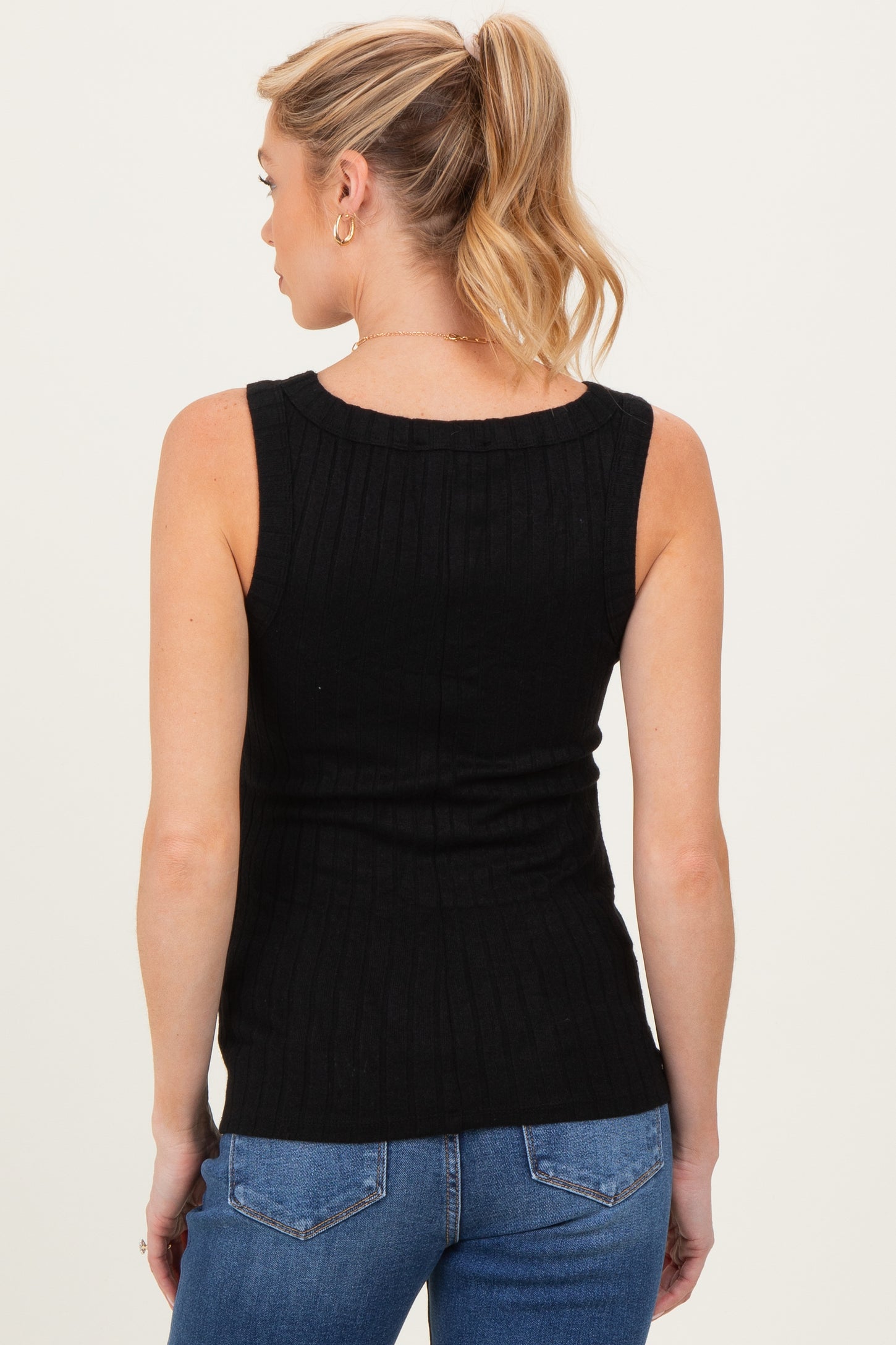woman wearing a black ribbed sleeveless maternity top with a fitted silhouette and back view, styled with jeans