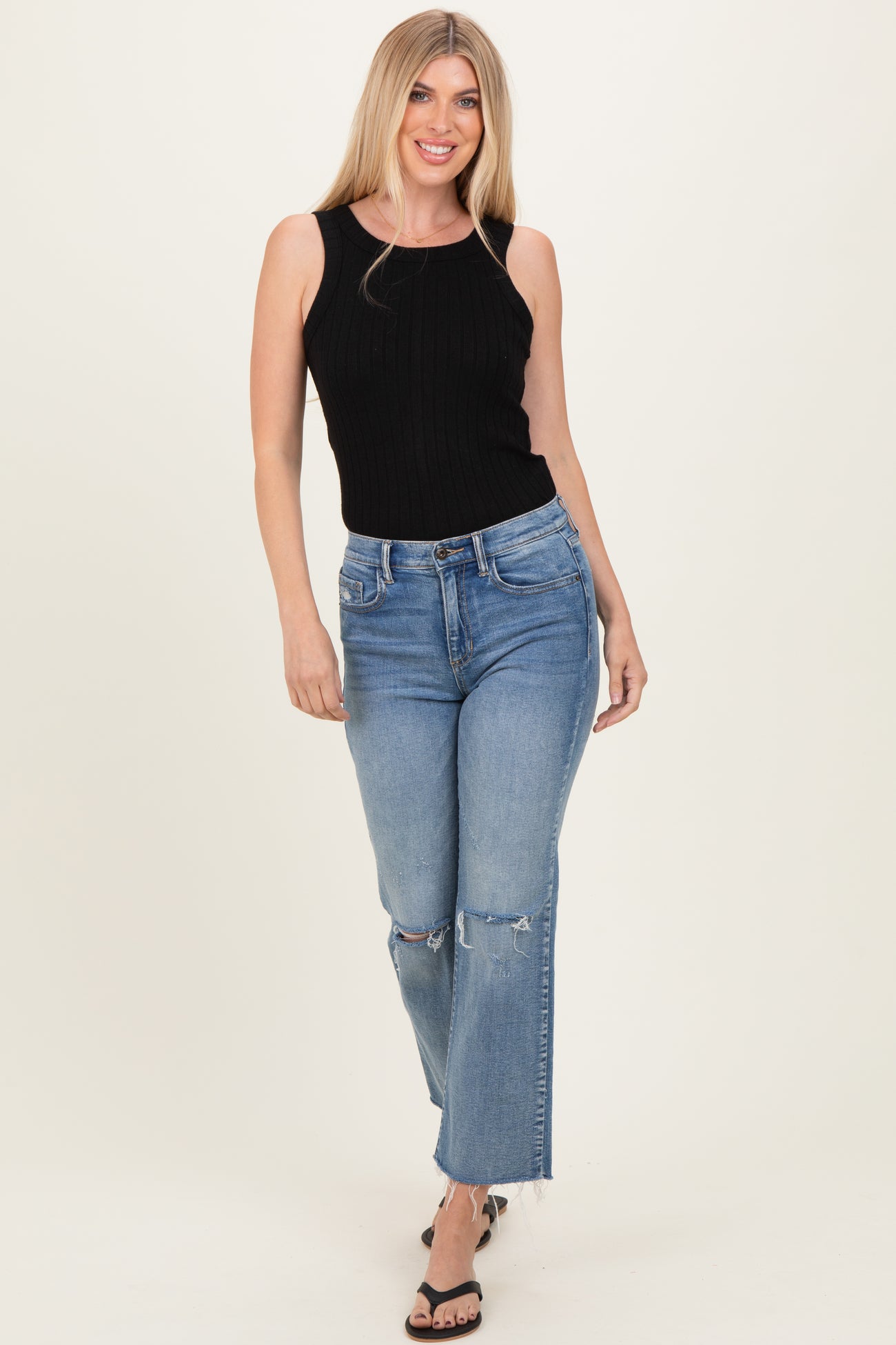 woman wearing a black ribbed tank top and distressed light blue straight-leg jeans, standing and smiling