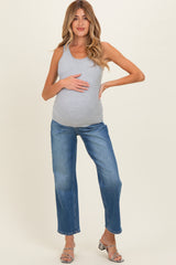 woman wearing a gray maternity tank top and blue jeans, cradling her baby bump