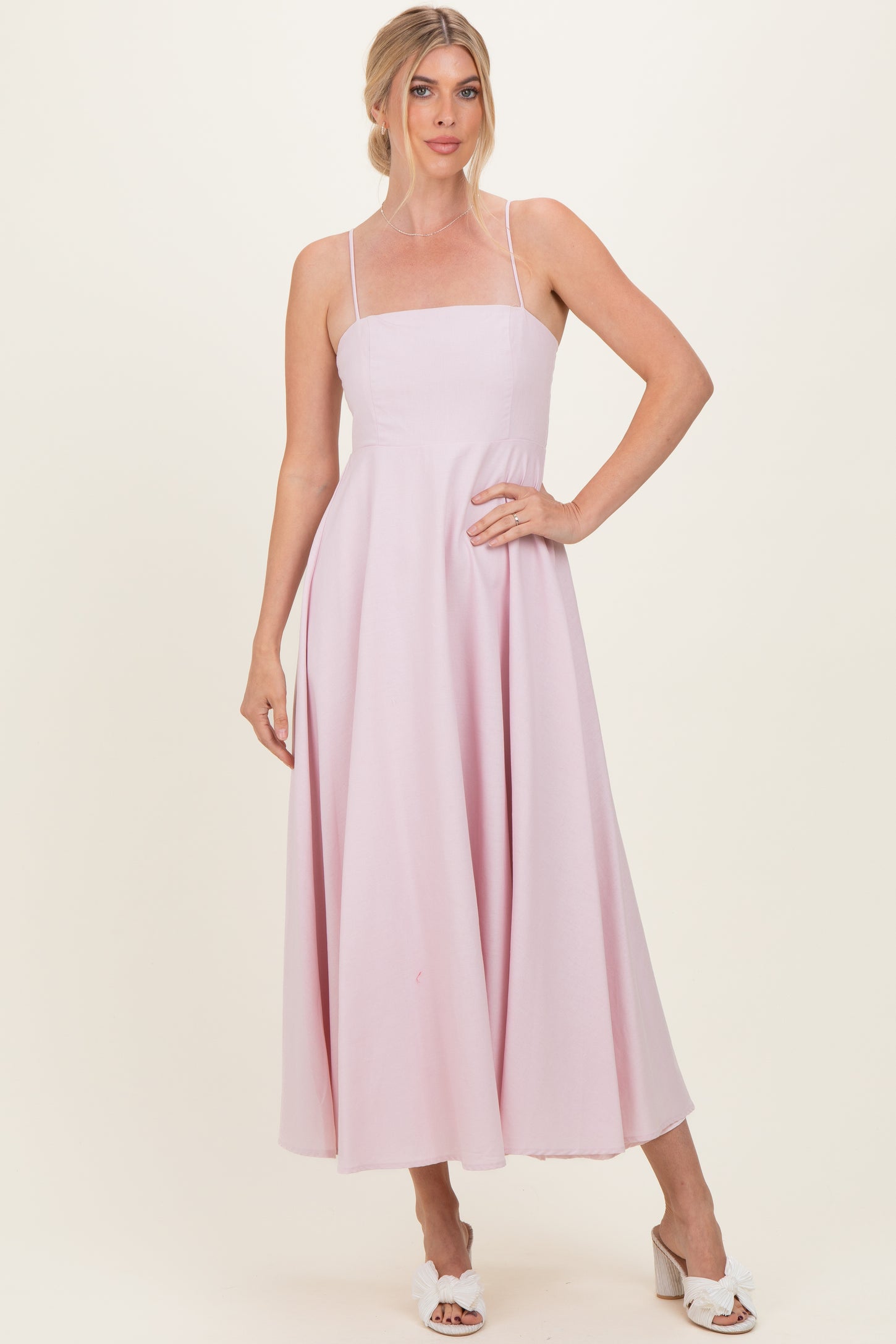 woman wearing a light pink spaghetti strap midi dress with a fitted bodice and flowy skirt
