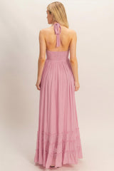 woman wearing a pink halter neck maxi dress with a smocked bodice and ruffled hem, showing the back view
