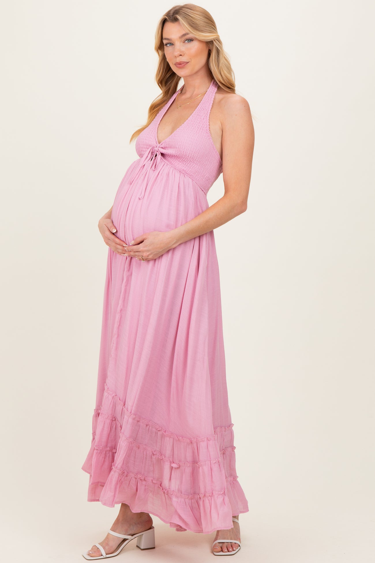 woman wearing a light pink halter neck maternity maxi dress holding her baby bump