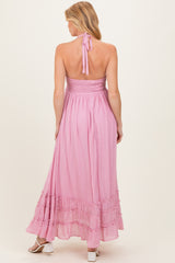 woman wearing a pink halter neck maternity maxi dress with a smocked bodice and ruffled hemline