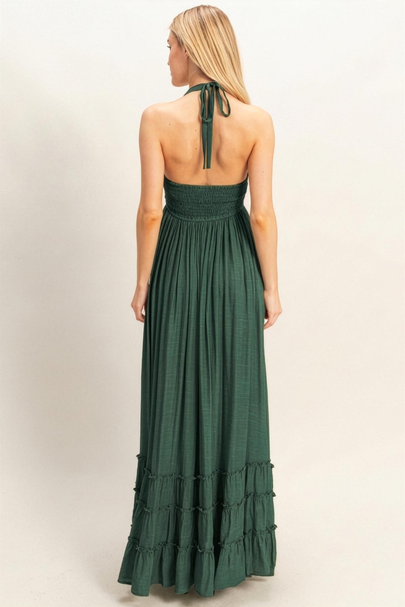 back view of a woman wearing a dark green maxi dress with a smocked bodice and tiered ruffle hem