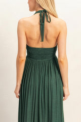 woman wearing a green halter neck maxi dress with a smocked bodice and a flowing skirt, viewed from the back