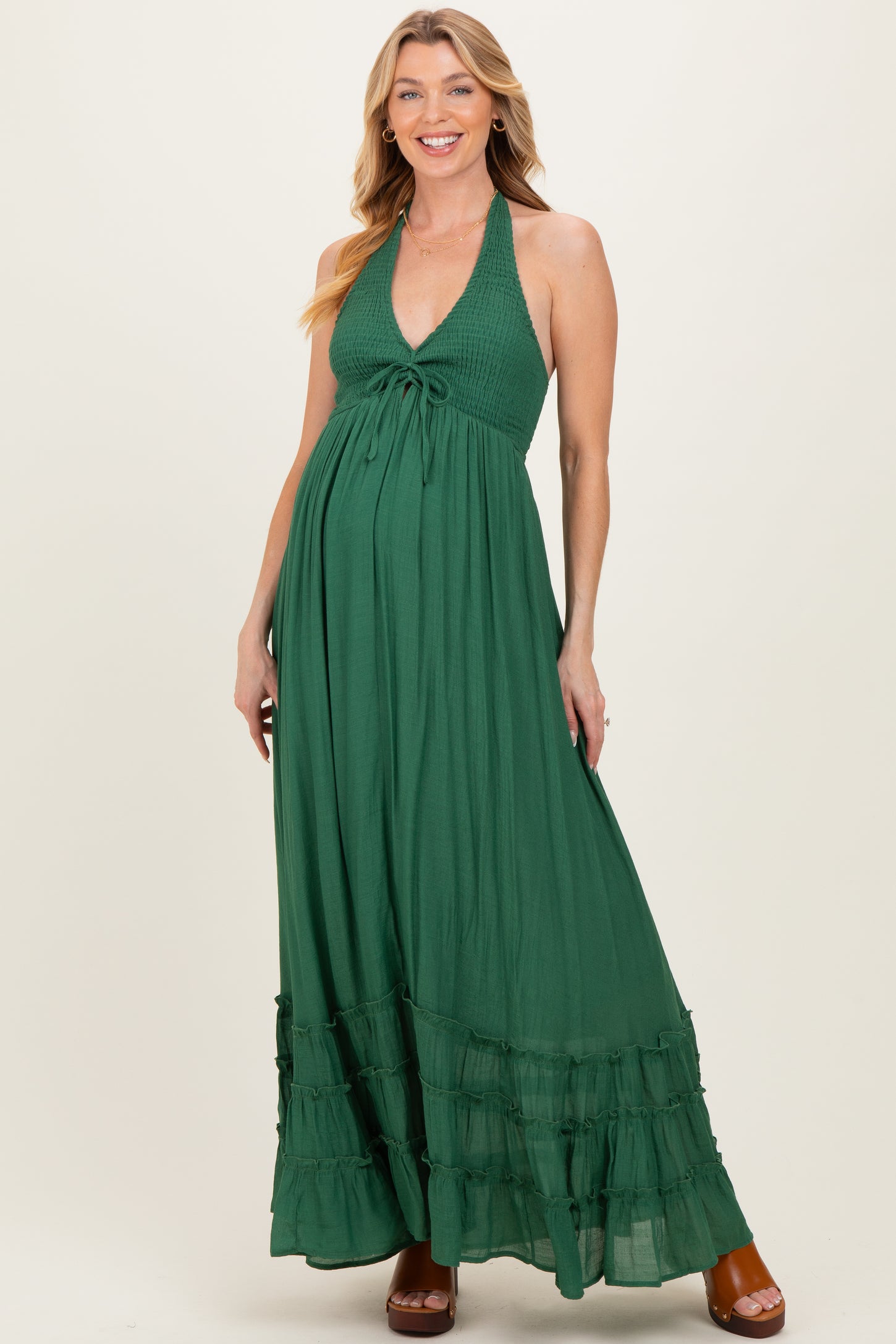woman wearing a green halter maternity maxi dress with a tie detail and ruffle hem, showcasing her baby bump