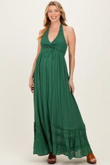 woman wearing a green halter maternity maxi dress with a tie detail and ruffle hem, showcasing her baby bump