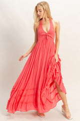 woman wearing a coral maxi dress with a halter neckline, tie detail, and ruffled hem