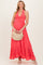 woman wearing a coral maternity maxi dress with a halter neck and tiered ruffle hem, holding a straw bag and showing her baby bump