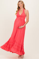 woman wearing a coral maternity maxi dress with halter neck and tiered ruffle hem, gently cradling her baby bump