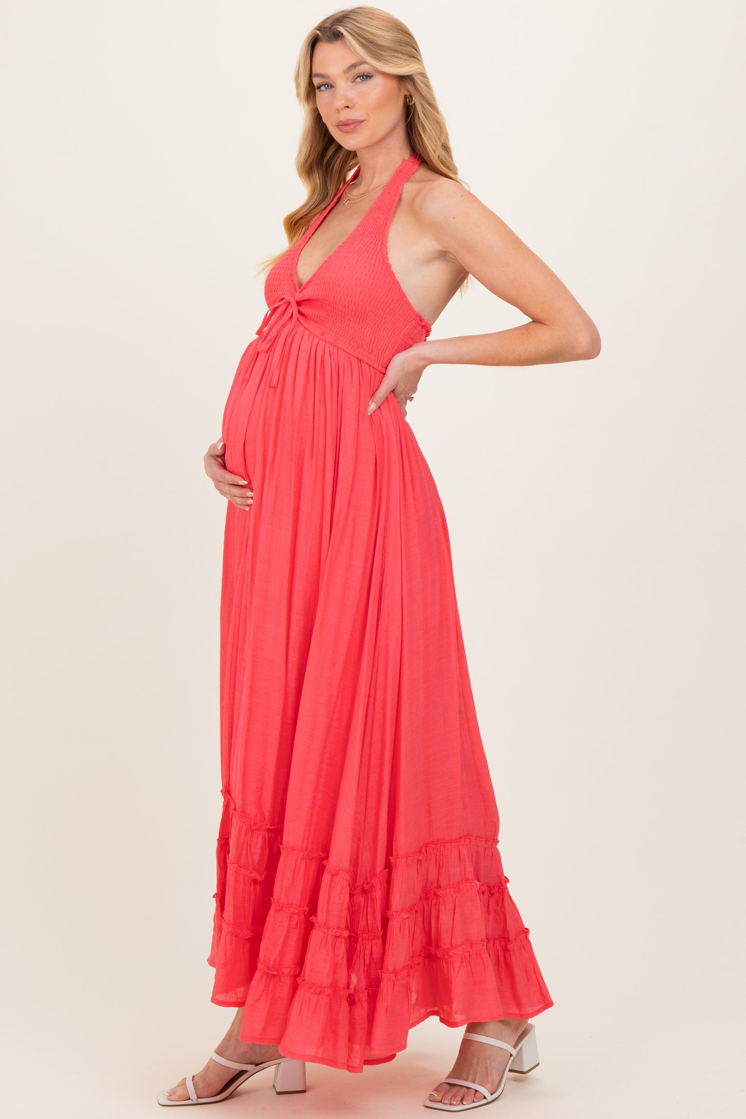 woman wearing a coral maternity maxi dress with a halter neck and ruffle hem, holding her baby bump