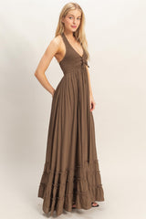 woman wearing a brown maxi dress with a smocked bodice and ruffled hem, posing with hands in pockets
