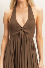 woman wearing a brown halter neck maxi dress with smocked bodice and a front tie detail
