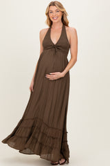 woman wearing a brown maternity maxi dress with a halter neck and ruffle details, gently cradling her baby bump