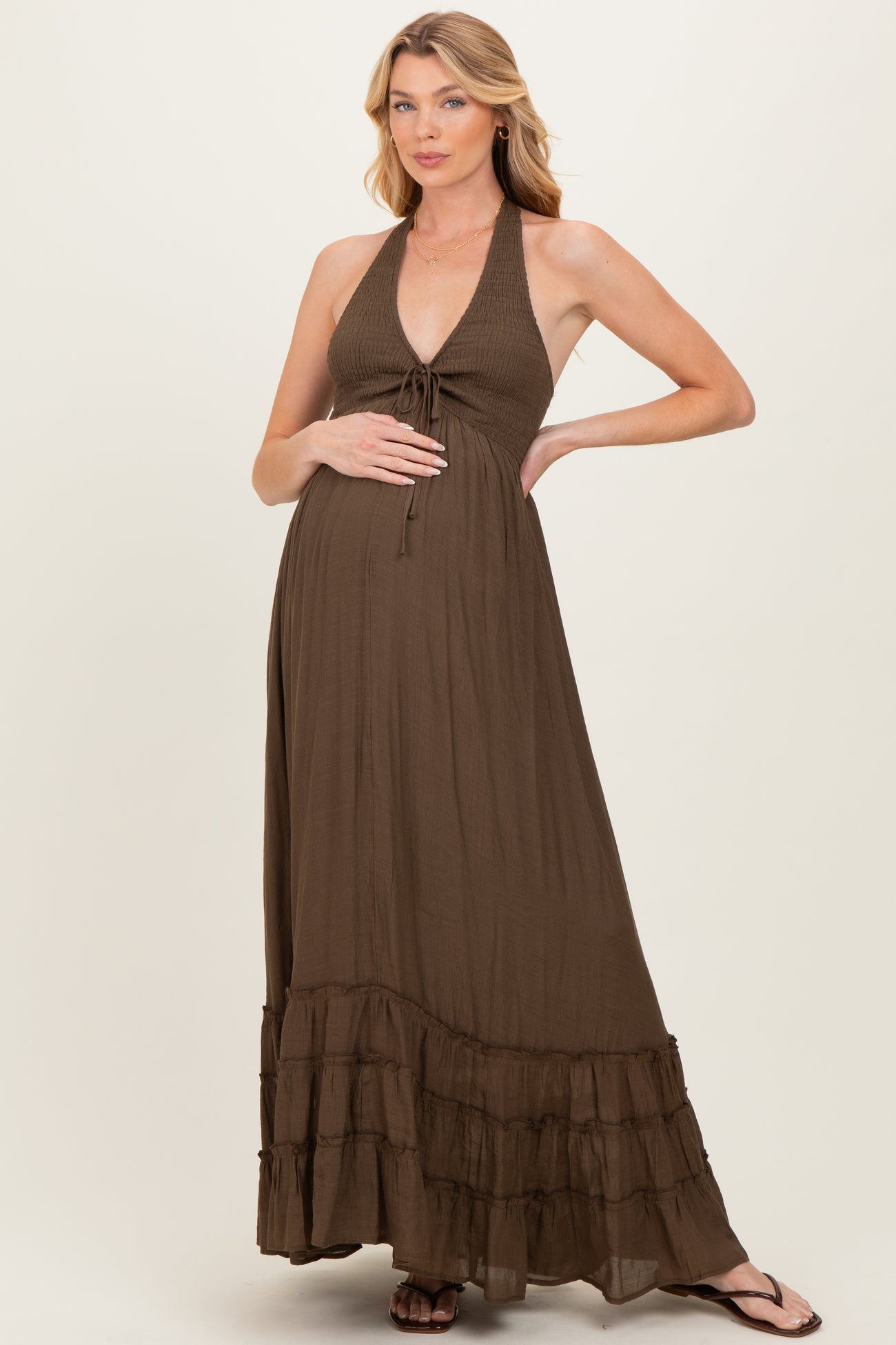 woman wearing a brown halter maternity maxi dress with tiered ruffle details and holding her baby bump